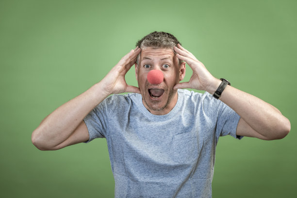 红色小丑鼻子的男人在绿色背景前面图片下载