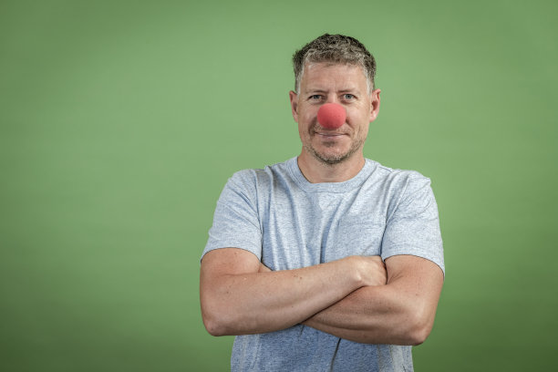 红色小丑鼻子的男人在绿色背景前面图片下载