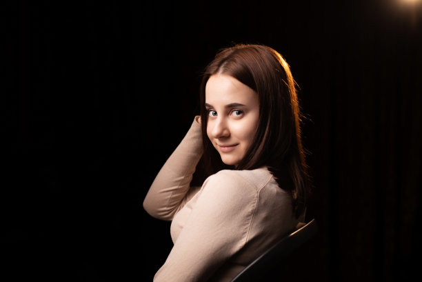 一个年轻女人的肖像在黑暗的背景上。那个穿棕色毛衣的女孩。友好的脸看着镜头。图片下载
