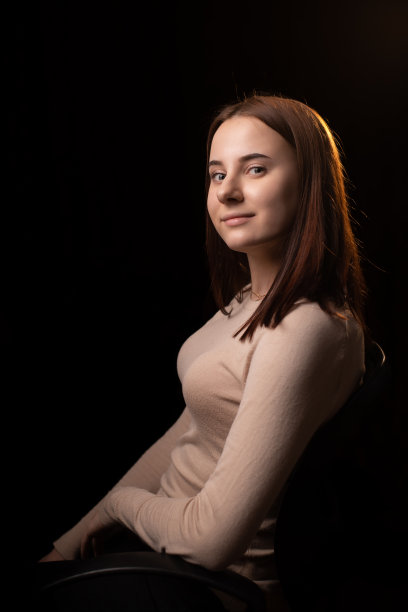 一个年轻女人的肖像在黑暗的背景上。那个穿棕色毛衣的女孩。友好的脸看着镜头。图片下载