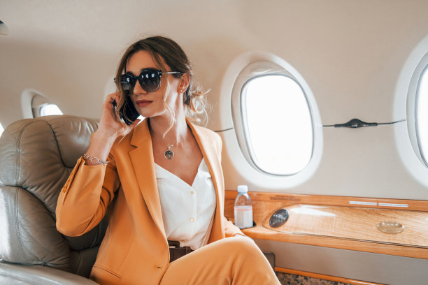 使用手机。穿着黄色衣服的年轻女乘客正在飞机上飞行图片下载