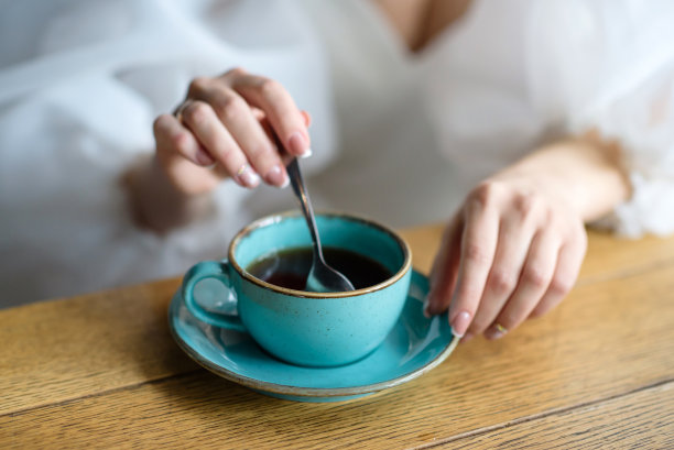 女孩在一杯咖啡里搅拌糖。热饮杯的特写非常浅的景深。图片下载