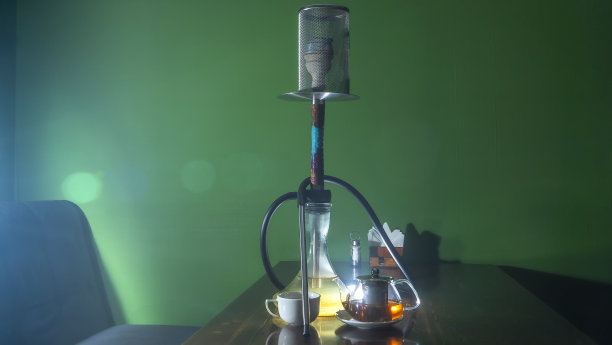 传统的阿拉伯水烟和带镜头光晕的茶。一壶茶和正在吸烟的水烟在深绿色的背景。图片下载