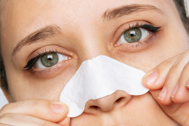 裁剪的镜头，一个女人的脸清洁她的鼻子皮肤与条状黑头图片下载