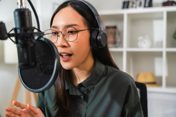 女人用麦克风，戴耳机，用笔记本录制播客。内容创造者的概念。图片下载