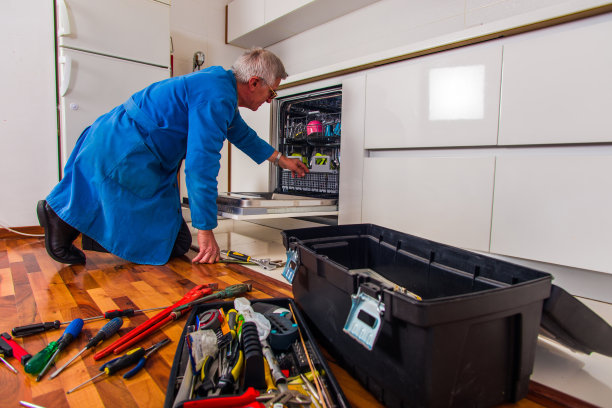 一个年老的工人正用身边的一堆工具打开洗碗机图片下载