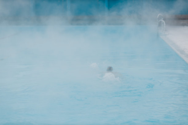 健康的游泳运动员男性训练游泳在开放的冬季游泳池与雾。地热户外spa概念，图片下载