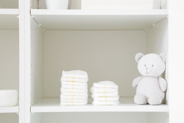 衣柜里白色的架子上堆放着新的婴儿尿布和柔软的泰迪熊。特写镜头。前视图。图片下载