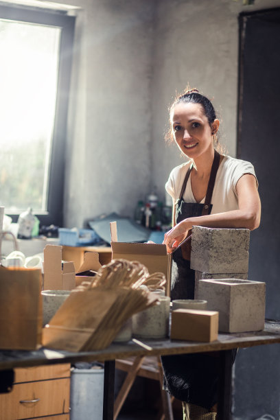 穿着围裙的手工艺人在她的工作室制作装饰混凝土花瓶。图片下载