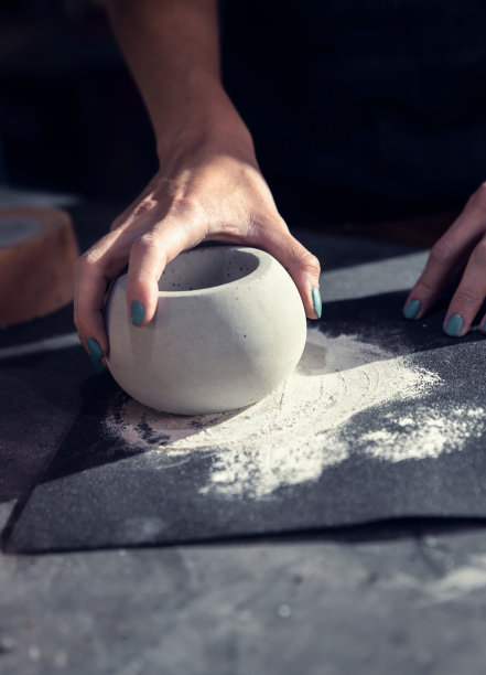 近距离拍摄手工艺人的手在她的工作室制作装饰混凝土花瓶。图片下载