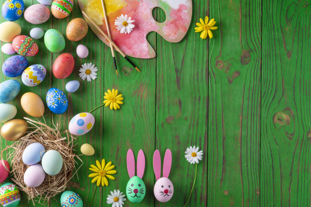 复活节彩蛋五颜六色的手画在绿色的木头上，上面点缀着雏菊花图片下载