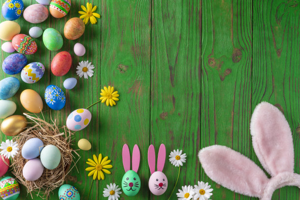 复活节彩蛋五颜六色的手画在绿色的木头上，上面点缀着雏菊花图片下载