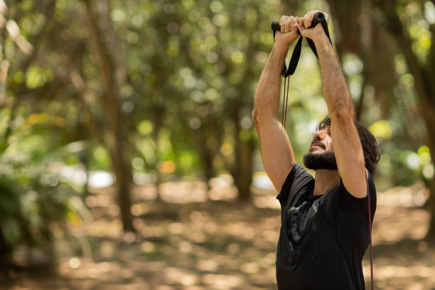 一个强壮的男人在户外的公园里用橡皮筋锻炼。男性运动员在锻炼时使用额外的运动器材。高质量的照片图片下载