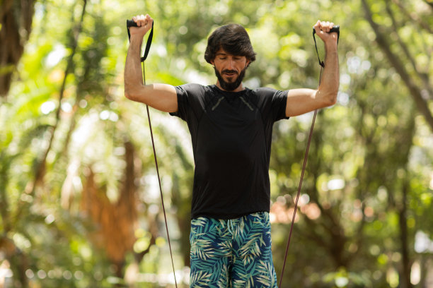 一个强壮的男人在户外的公园里用橡皮筋锻炼。男性运动员在锻炼时使用额外的运动器材。高质量的照片图片下载