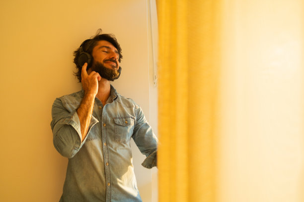 侧视图的年轻人听音乐，耳机在他的耳朵边的窗户，看着外面的城市景观的背景。高质量的照片图片下载