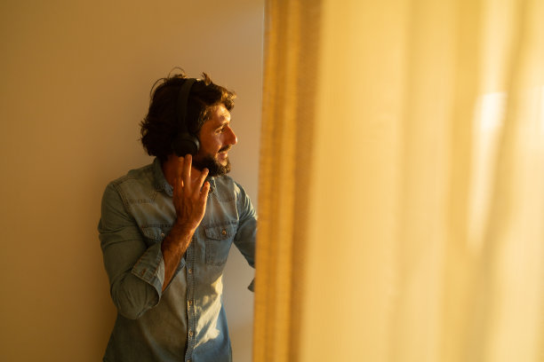 侧视图的年轻人听音乐，耳机在他的耳朵边的窗户，看着外面的城市景观的背景。高质量的照片图片下载