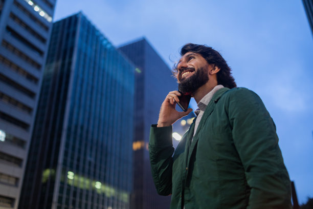 年轻人在夜晚使用智能手机的照片，背景是城市景观。高质量的照片图片下载