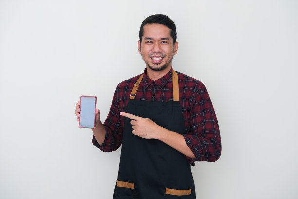 成年亚洲人穿着围裙，显示黑色的手机屏幕。快乐的表情图片下载