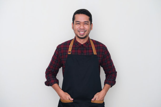 成年亚洲人穿着围裙，看着镜头，微笑着自信图片下载
