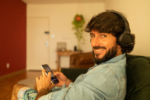 侧视图的年轻人听音乐与耳机在他的耳朵在窗口与城市景观的背景。高质量的照片图片下载