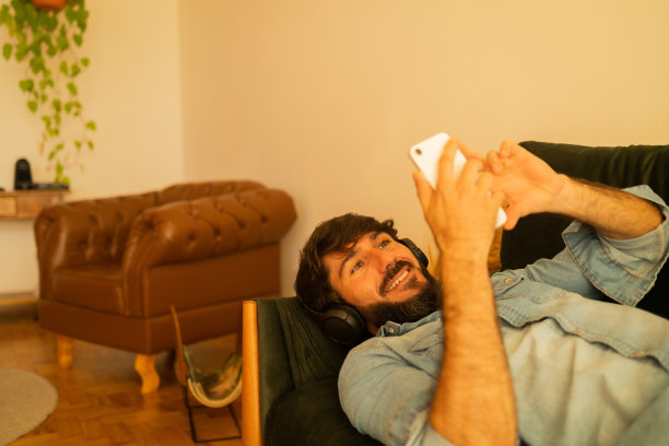 侧视图的年轻人听音乐与耳机在他的耳朵在窗口与城市景观的背景。高质量的照片图片下载