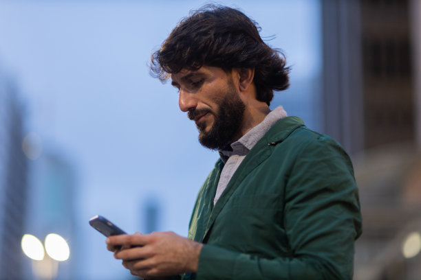 年轻人在夜晚使用智能手机的照片，背景是城市景观。高质量的照片图片下载
