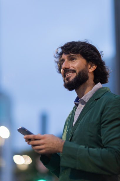 年轻人在夜晚使用智能手机的照片，背景是城市景观。高质量的照片图片下载