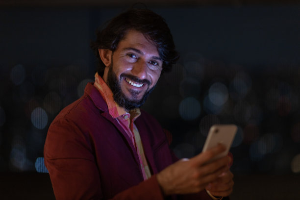 年轻人在夜间使用智能手机的侧视图，背景是城市景观。高质量的照片图片下载