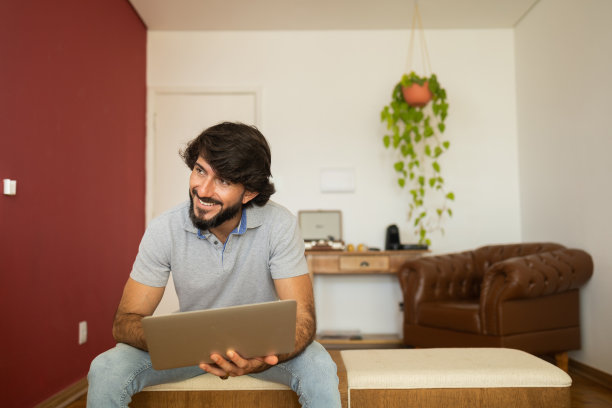 年轻的商人，坐在客厅的椅子上，大腿上放着笔记本电脑，在家工作。家庭办公室的概念。灰色的工作笔记本。家庭办公室的概念。高质量的照片图片下载