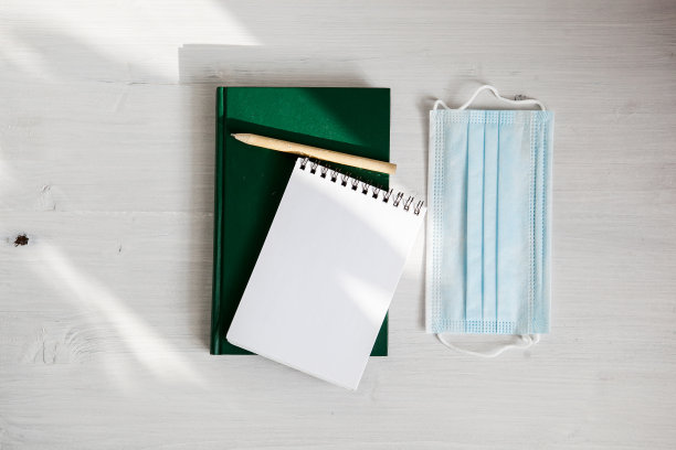 打开白色笔记本上的一个绿色日记本，一个医用口罩和一个绿色树枝图片下载