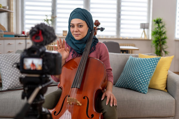 年轻的穆斯林妇女在家里演奏大提琴时拍摄视频图片下载