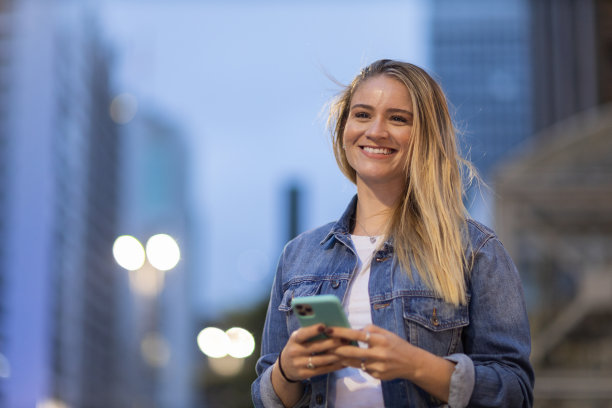 年轻人在夜晚使用智能手机的照片，背景是城市景观。高质量的照片图片下载