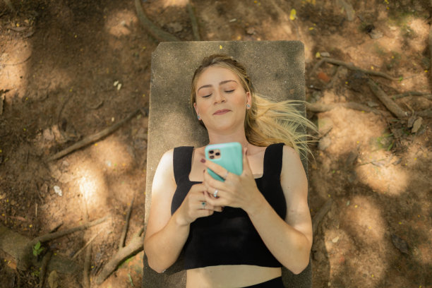 年轻人在白天使用智能手机，背景是一个绿色的公园。高质量的照片图片下载