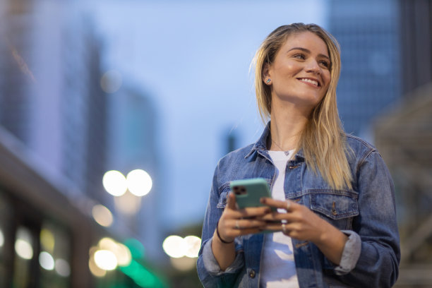 年轻人在夜晚使用智能手机的照片，背景是城市景观。高质量的照片图片下载