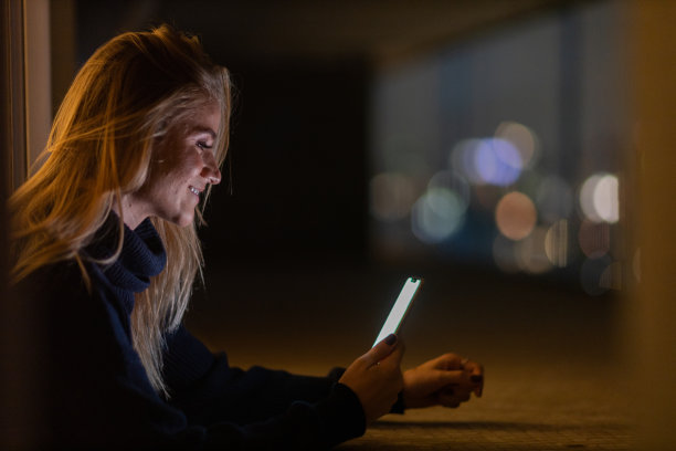 年轻人在夜晚使用智能手机的前视图，城市景观在背景中。高质量的照片图片下载