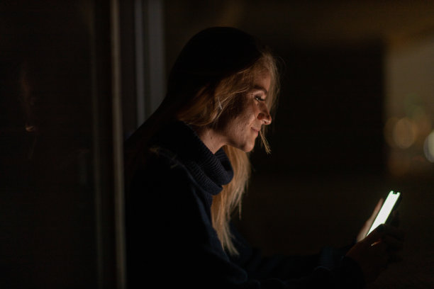 年轻人在夜晚使用智能手机的前视图，城市景观在背景中。高质量的照片图片下载