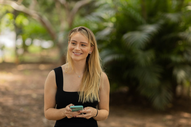 年轻人在白天使用智能手机，背景是一个绿色的公园。高质量的照片图片下载