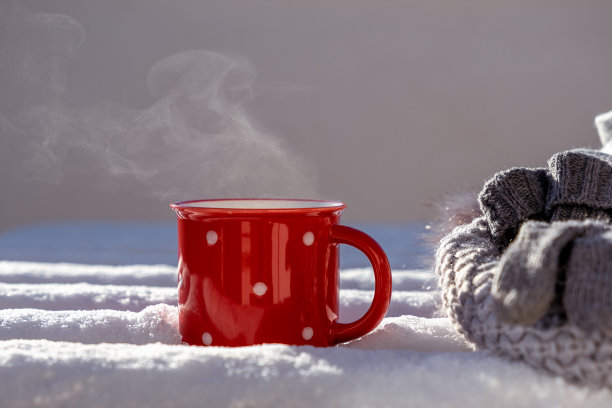 一杯红色的热气腾腾的茶，一顶帽子和手套在雪地里的桌子上图片下载