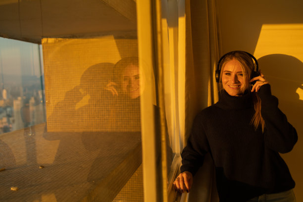 侧视图的年轻人听音乐与耳机在他的耳朵在窗口与城市景观的背景。高质量的照片图片下载