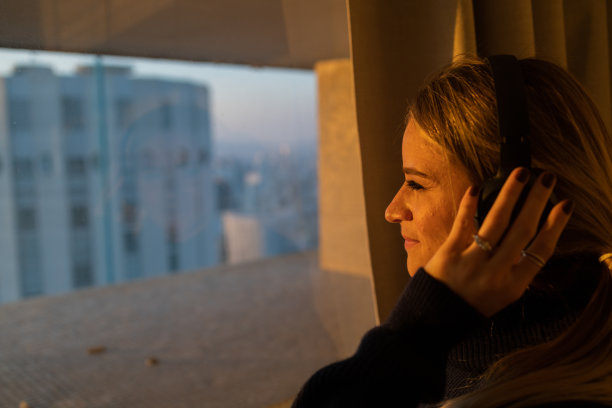 侧视图的年轻人听音乐与耳机在他的耳朵在窗口与城市景观的背景。高质量的照片图片下载