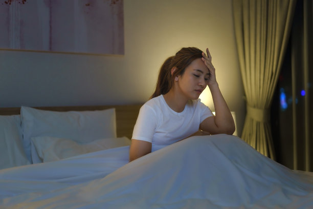 亚洲妇女躺在白色的床上在卧室里看起来担心或思考一些关于她的生活或工作在半夜在家里。图片下载