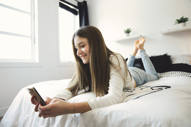 一个十几岁的女孩把智能手机放在床上图片下载