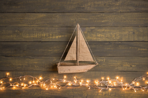 旅行和冒险创意概念-木制背景上的玩具船。圣诞彩灯像海浪图片下载
