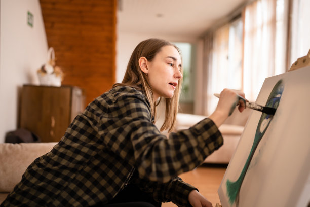 一位年轻美丽的白人女性艺术家坐在床上沙发在画布上绘画，拿着画笔艺术和创意专业或爱好概念真实的人侧视复制空间图片下载