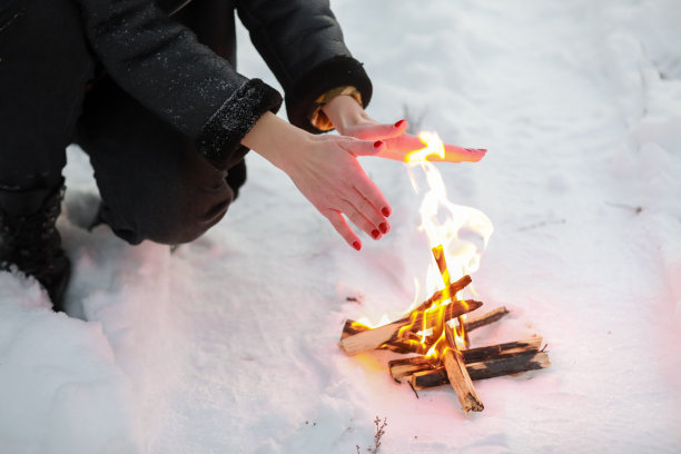 裁剪照片的年轻女子在冬季森林的篝火上温暖她的手。特写镜头图片下载