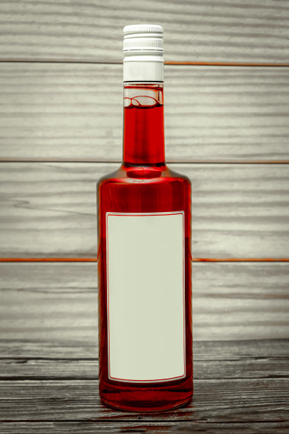 酒瓶与红色饮料和空白白色标签在木制背景。本空间图片下载