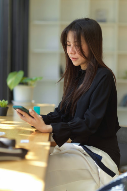 一名亚洲年轻女性坐在咖啡馆里用智能手机打字的照片。图片下载