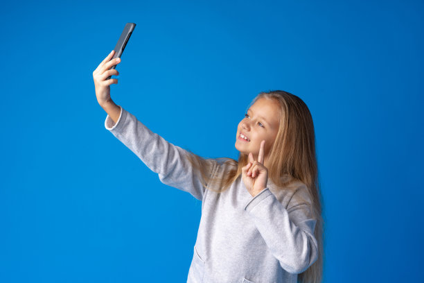 一个兴奋的小女孩在蓝色背景下自拍的肖像图片下载