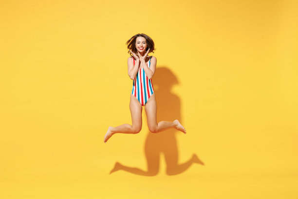 全长乐趣快乐年轻女子苗条的身体穿条纹红蓝色连体泳衣跳高空中跑飞孤立在鲜艳的黄色背景工作室夏季酒店泳池海休息太阳概念图片下载