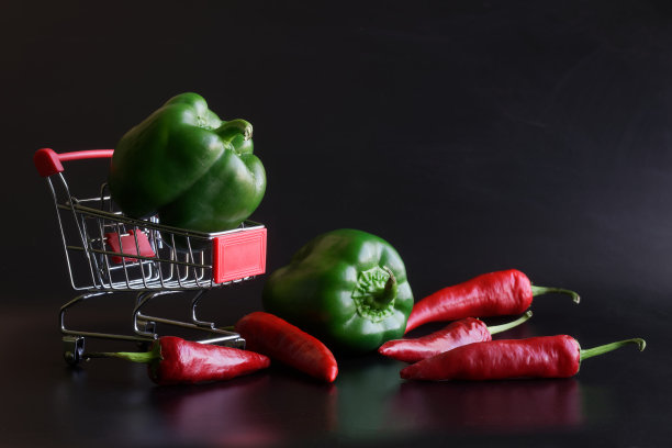 超市手推车上的红辣椒和青椒呈深色渐变背景。出售和购买香料和调味品的概念图片下载